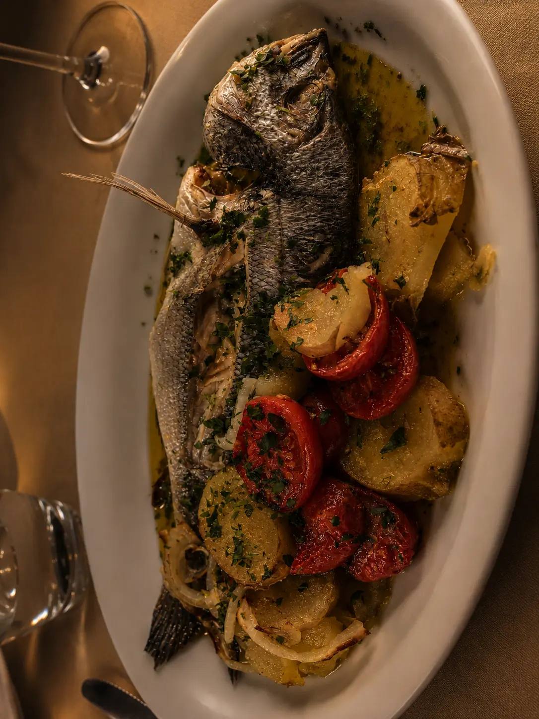Pesce intero al forno servito con patate e pomodorini, in tavola